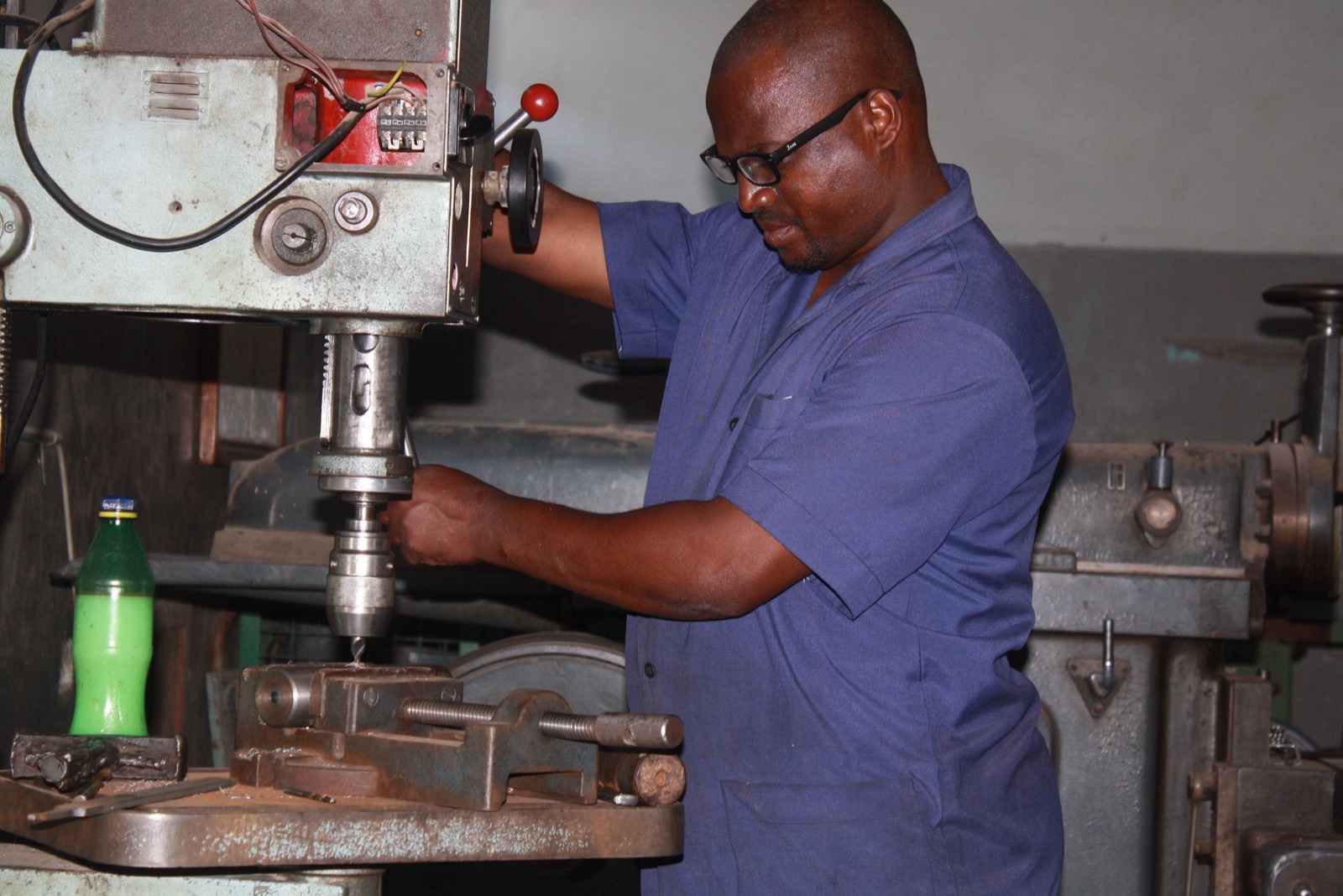 An instructor operating a pillar drill in the mechanical workshop
